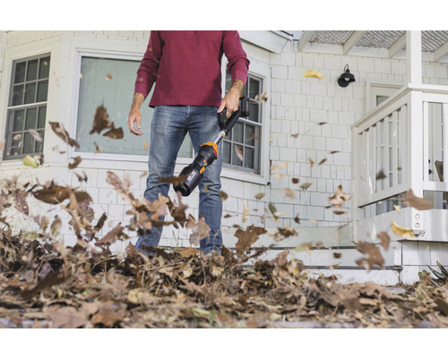 Un homme utilise un souffleur de feuilles pour enlever les feuilles devant une maison.
