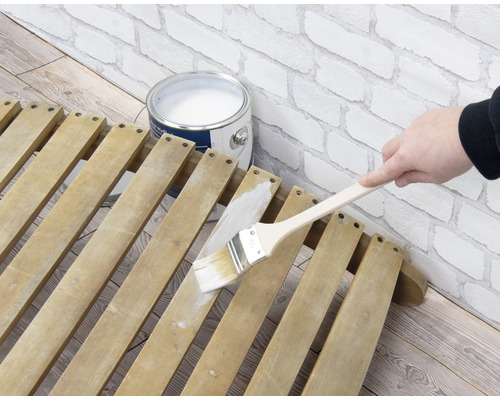 Anstreichen eines Holzlattenrostes mit einem Pinsel und Farbe neben einer Farbdose