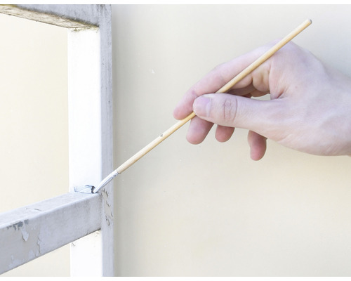 Une main peint une grille métallique avec un pinceau