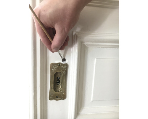 Peinture d''une porte blanche au pinceau près d''un trou de serrure