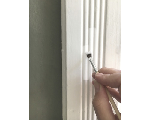 Une personne peint une moulure blanche avec un pinceau.