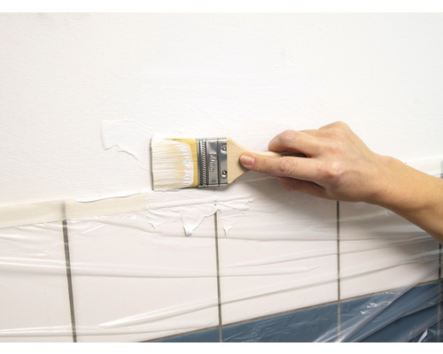 Une personne peint un mur au-dessus de carreaux recouverts d''un film de protection avec un pinceau.