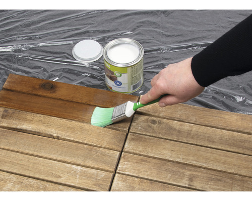 Une personne peint des carreaux de bois avec un pinceau et une lasure de protection du bois.