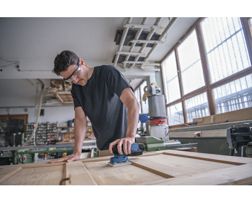 Mann schleift Holztür mit einem Elektroschleifer in einer Werkstatt.