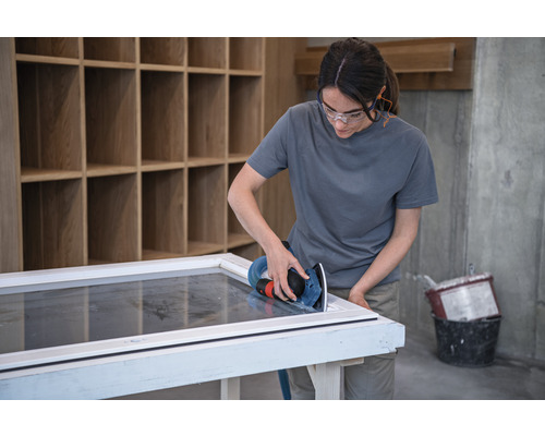 Frau schleift Fensterrahmen mit einem Exzenterschleifer