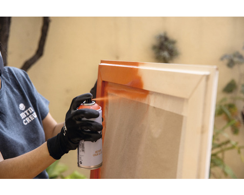 Une personne vaporise de la peinture sur un cadre en bois avec un aérosol.