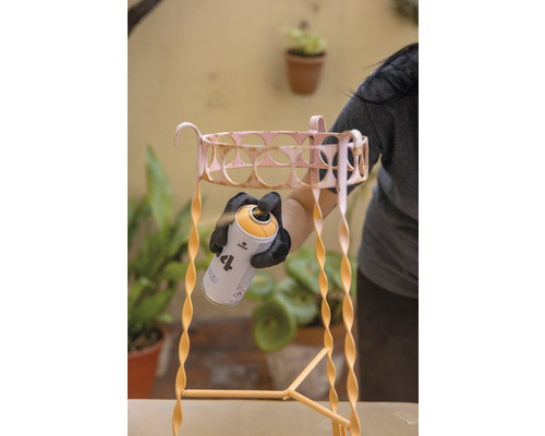 Une personne vaporise un escabeau pour plantes en métal avec une peinture en aérosol. L''escabeau pour plantes a une conception en spirale.