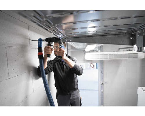 Un homme perce un trou dans un mur avec un perforateur et un dispositif d''aspiration