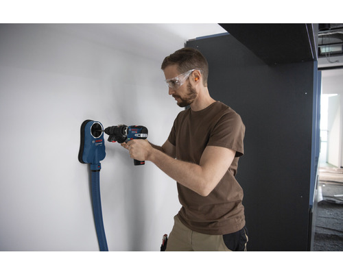 Un homme perce un trou dans un mur avec une perceuse-visseuse sans fil, à l''aide d''un dispositif d''aspiration de poussière Bosch