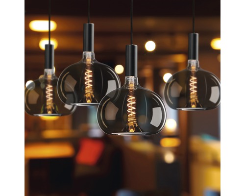 Mehrere Pendelleuchten mit Glühfaden im Retrodesign hängen im Raum.