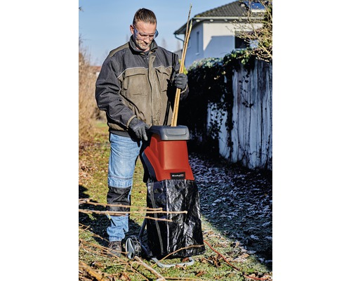 Eine Person benutzt einen Häcksler im Garten zum Zerkleinern von Ästen und Zweigen.