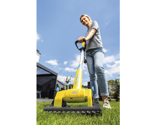 Frau benutzt eine Gloria Multibürste auf Rasen für die Gartenpflege.