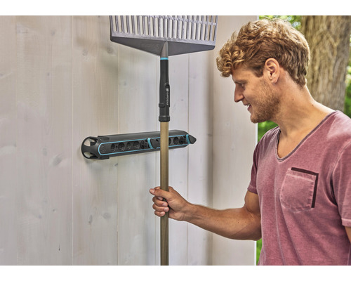 Un homme accroche un râteau dans un support à outils sur un mur