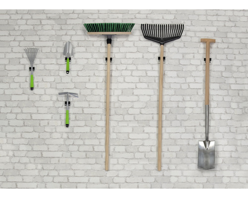 Des outils de jardinage tels que balai, râteau, pelle et houe sont accrochés à un mur