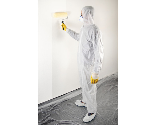 Personne en combinaison de protection peignant un mur avec un rouleau à peinture