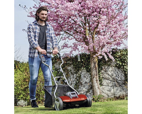 Une personne utilise un scarificateur dans le jardin devant un arbre en fleurs.