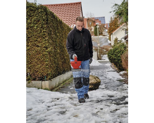 Mann entfernt Schnee mit einer Schneefräse von einem Gehweg