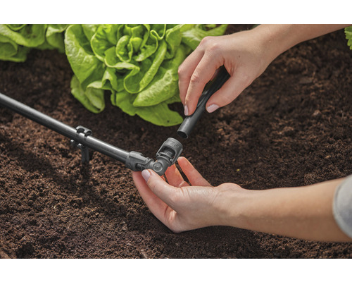 Scène de jardin avec système d''irrigation et personne fixant un raccord.
