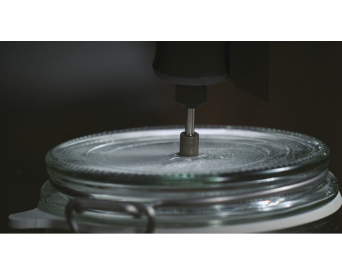 Un outil perce un trou dans le couvercle d''un bocal.