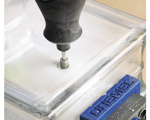 Ein Werkzeug bohrt ein Loch in einen Glasbaustein, der in einem Schraubstock fixiert ist