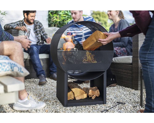 Groupe de personnes assises autour d''un foyer en métal avec rangement pour le bois dans le jardin.