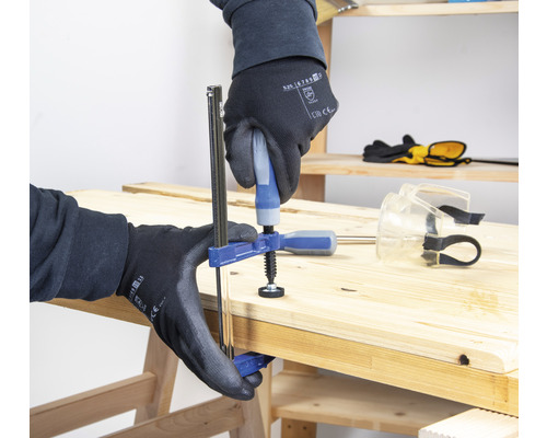 Eine Person befestigt ein Werkstück mit einer Einhandzwinge auf einer Holzwerkbank.