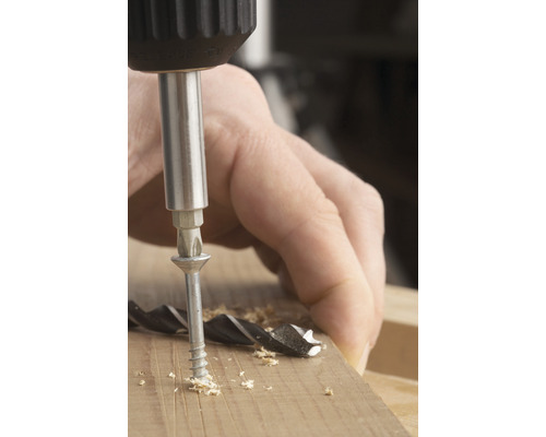 Une vis est vissée dans un morceau de bois avec un tournevis.