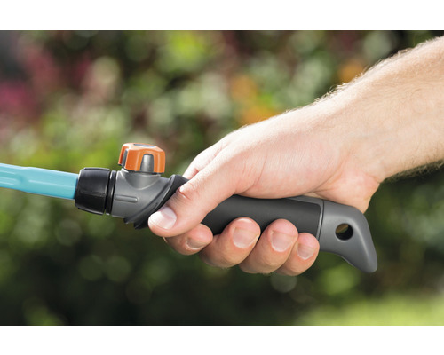 Une main tient un tuyau d''arrosage avec vanne d''arrêt.