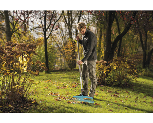 Un homme ratisse les feuilles mortes dans un jardin avec un râteau.