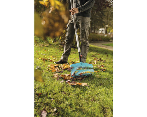 Une personne ratisse les feuilles mortes avec un râteau à feuilles sur une pelouse.