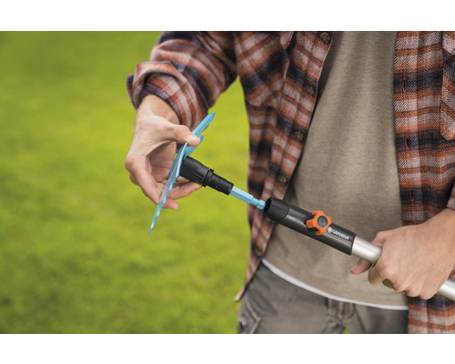 Une personne fixe un accessoire d''arrosage de jardin Gardena sur un tuyau d''arrosage.