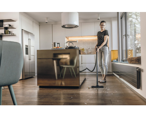 Frau saugt Glasscherben mit Staubsauger in der Küche auf