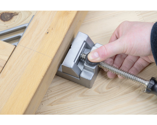 Eine Person fixiert zwei Holzstücke mit einer Winkelspannzwinge.