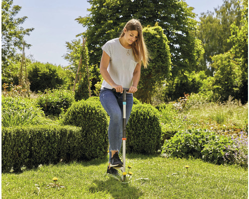 Une femme enlève les mauvaises herbes dans le jardin avec un désherbeur.
