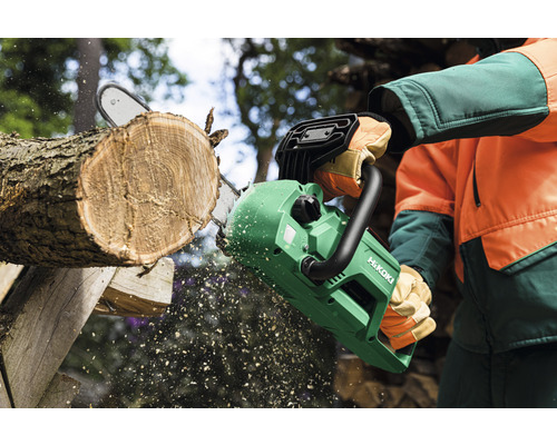 Eine Person sägt mit einer Akku-Kettensäge einen Baumstamm. HiKoki Logo.