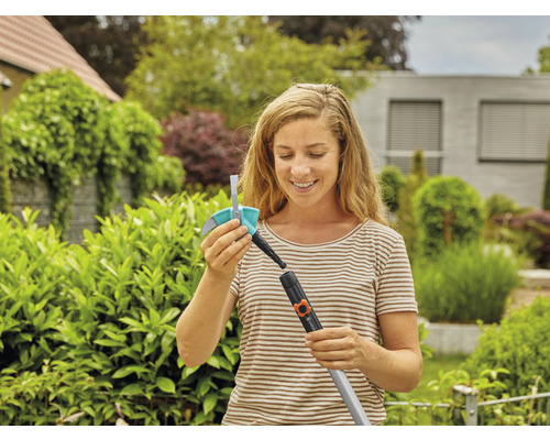 Une femme fixe un accessoire d''arrosage à une douche de jardin Gardena dans le jardin.