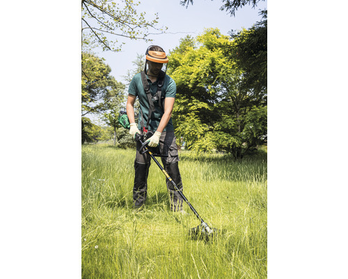 Mann mäht Gras mit einem Rasentrimmer im Garten.