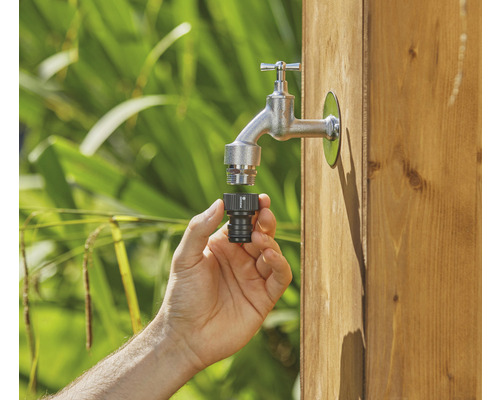 Une main raccorde un connecteur de robinet à un robinet de jardin.