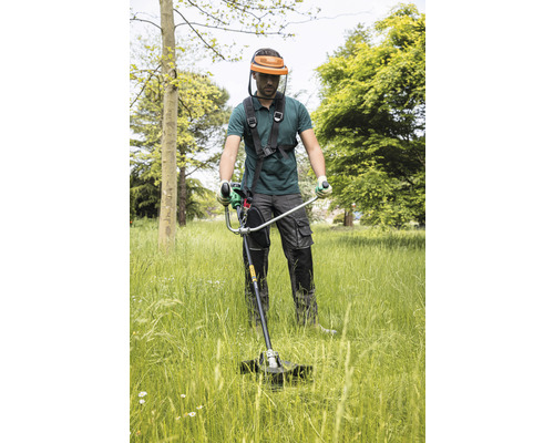 Mann mit Schutzvisier, der mit einem Rasentrimmer Gras schneidet