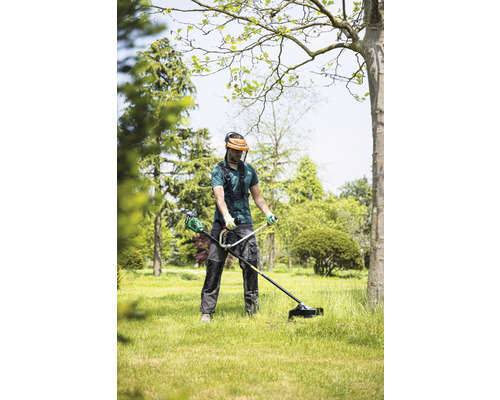 Mann mit Gesichtsschutz und Trimmer beim Rasentrimmen im Garten.