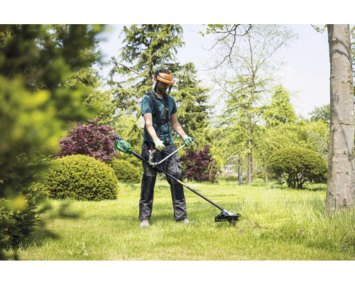 Mann verwendet Rasentrimmer im Garten mit Bäumen und Sträuchern.