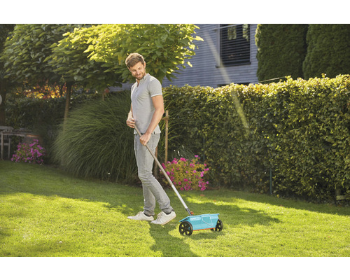 Un homme utilise un épandeur dans le jardin pour l''entretien de la pelouse.