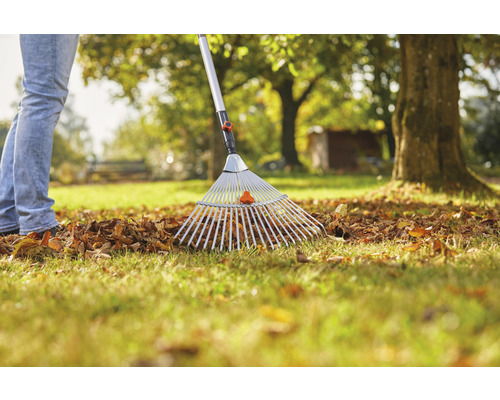 Une personne ratisse les feuilles avec un râteau à feuilles dans le jardin.