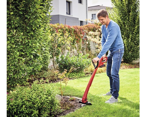 Mann benutzt einen Rasentrimmer im Garten, um Rasenkanten zu schneiden.