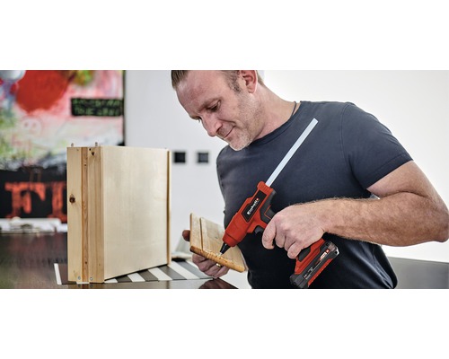 Mann verwendet eine Heissklebepistole zum Zusammenfügen von Holzteilen.