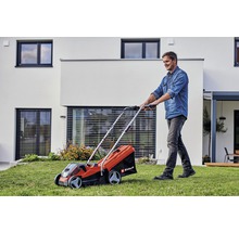 Un homme utilise une tondeuse à gazon Einhell dans le jardin devant une maison.