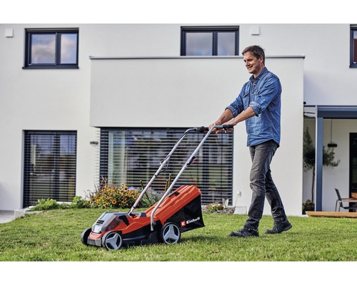 Un homme utilise une tondeuse à gazon Einhell dans le jardin devant une maison.