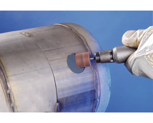 Eine Person mit Handschuhen benutzt einen Rotationsschleifer an einem Metallbehälter.