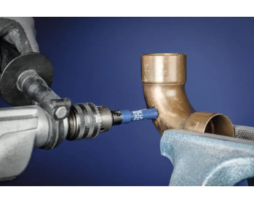 Une scie cloche perce un trou dans un tuyau de cuivre fixé dans un étau