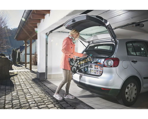 Frau verstaut eine Transportkarre im Kofferraum eines Autos in einer Garage.